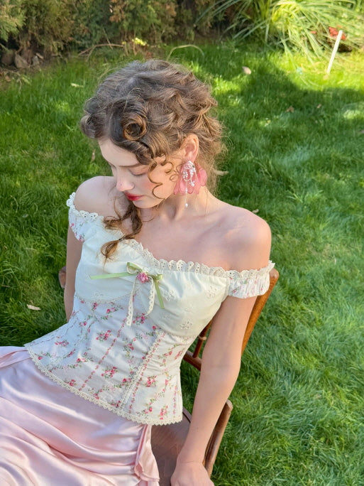Romantic floral off-shoulder corset top styled with a pink satin skirt, photographed outdoors on green grass – vintage fairytale fashion for women