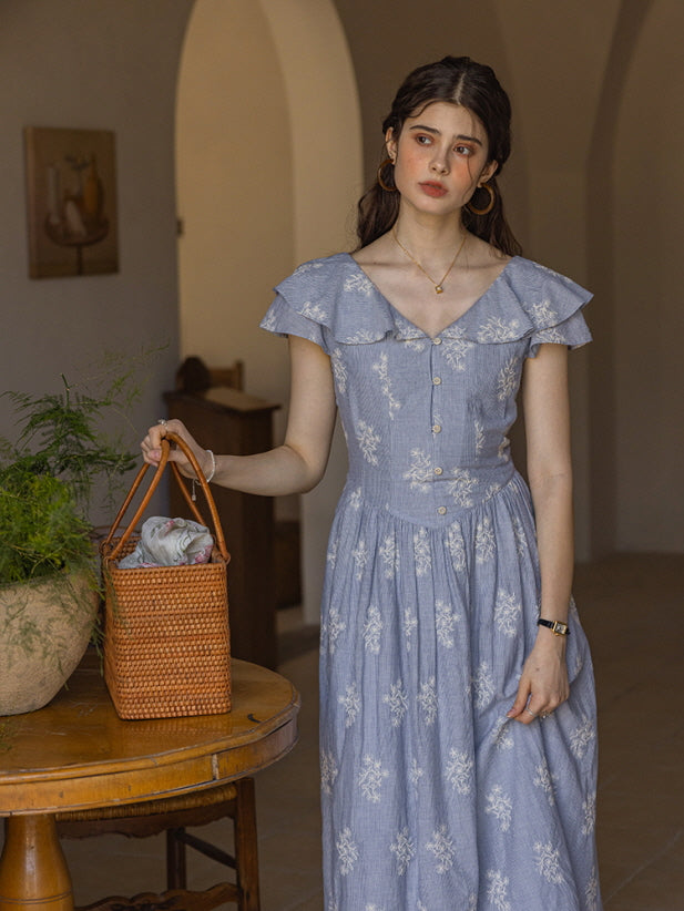 Charming light blue cotton dress with delicate white floral embroidery and ruffled cap sleeves, styled with a woven basket bag in a serene, cottage-inspired room.