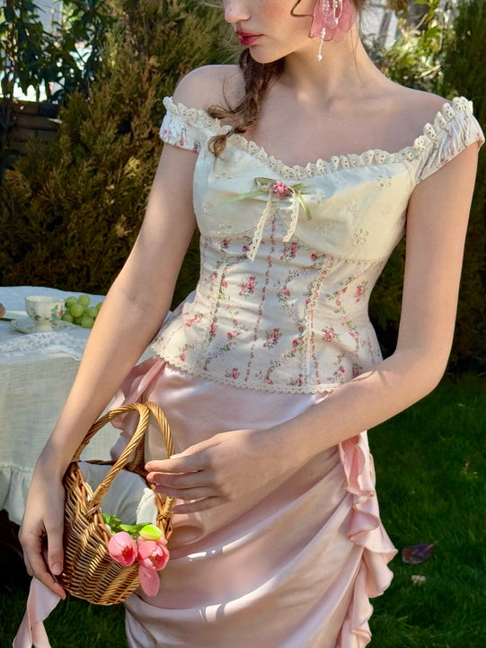 Close-up of floral lace corset top with ribbon bow, paired with pastel pink ruched satin skirt and a wicker basket – romantic cottagecore outfit in spring garden setting