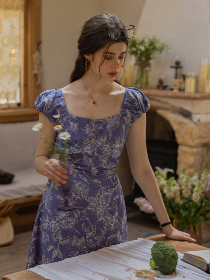 Young woman in a blue floral puff-sleeve dress holding a daisy-filled glass, set in a rustic cottage kitchen with stone accents and wildflower decor, capturing a dreamy cottagecore vibe.