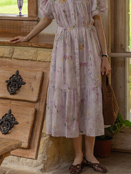 Close-up of the floral dress, showcasing the delicate watercolor-style floral pattern in soft pastel hues of pink, lavender, and green. The model holds a woven brown bag, capturing a nostalgic vintage-inspired look.