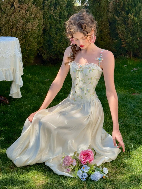 Romantic cream balloon skirt paired with floral embroidered corset top, sitting on grass with pastel flower bouquet – fairytale-inspired feminine spring fashion look