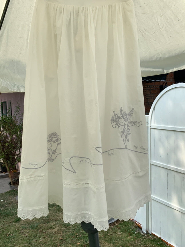 White vintage-style midi skirt with delicate angel embroidery and scalloped hem, displayed outdoors in a bright and natural setting, showcasing its light and flowy aesthetic.