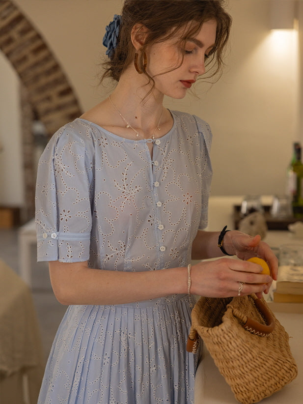Close-up of a woman placing lemons into a woven basket while wearing a blue eyelet lace dress with delicate floral patterns. Cottagecore aesthetic.