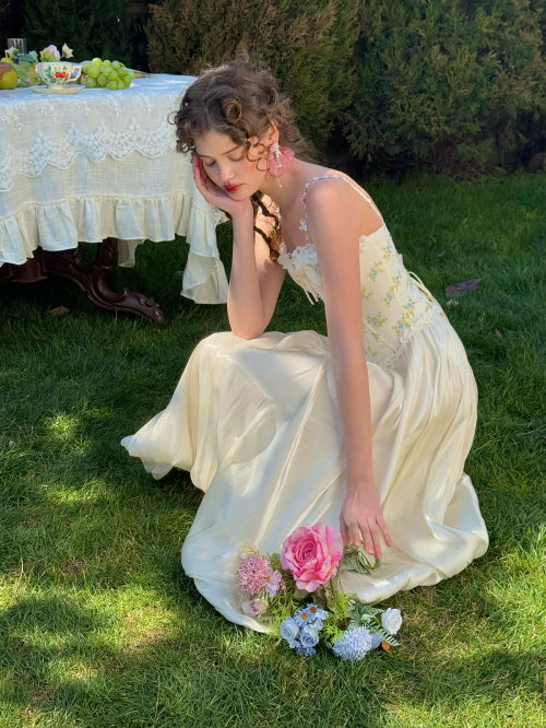 Cream balloon skirt styled with floral embroidered corset top, sitting on grass with pastel flower bouquet – romantic fairytale aesthetic for spring garden fashion