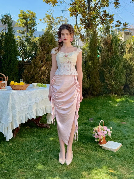 Romantic pink ruched satin midi skirt with asymmetric draping, styled with a floral corset top in a spring garden setting – fairytale-inspired vintage women’s outfit