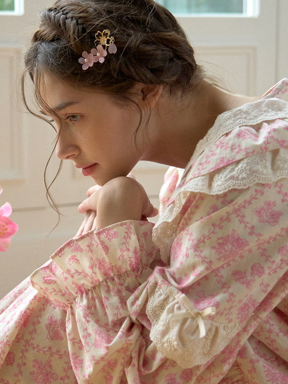 A delicate side profile of a model wearing a pink floral loungewear set with lace trim and a floral hairpin, evoking a soft, romantic atmosphere.