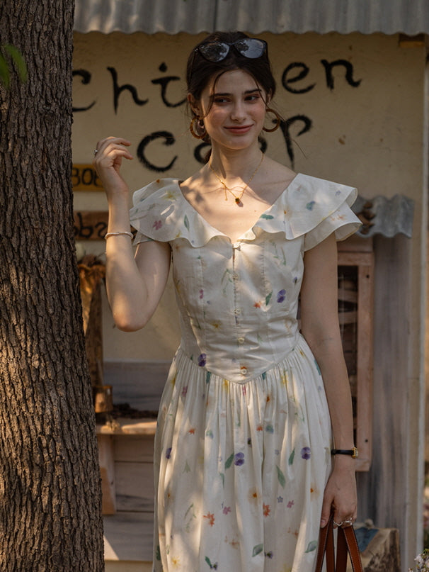 Close-up of a woman smiling while wearing a cottagecore-style floral dress with ruffled sleeves, standing in front of a rustic chicken coop backdrop.