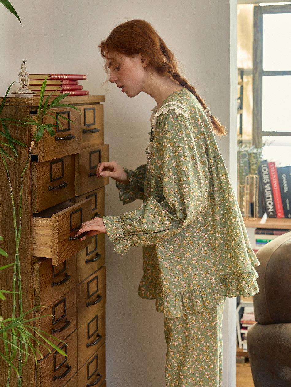 A whimsical scene with a model in a green floral loungewear set, opening a wooden drawer, styled in a nostalgic, fairytale-inspired look.