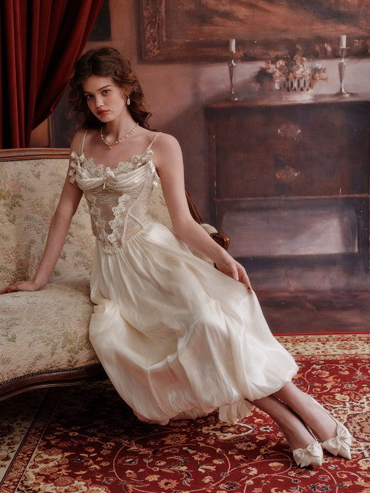 A romantic vintage-inspired cream lace corset dress with balloon skirt, worn by a model lounging gracefully on an antique floral sofa, styled in a fairytale aesthetic room with red velvet curtains.