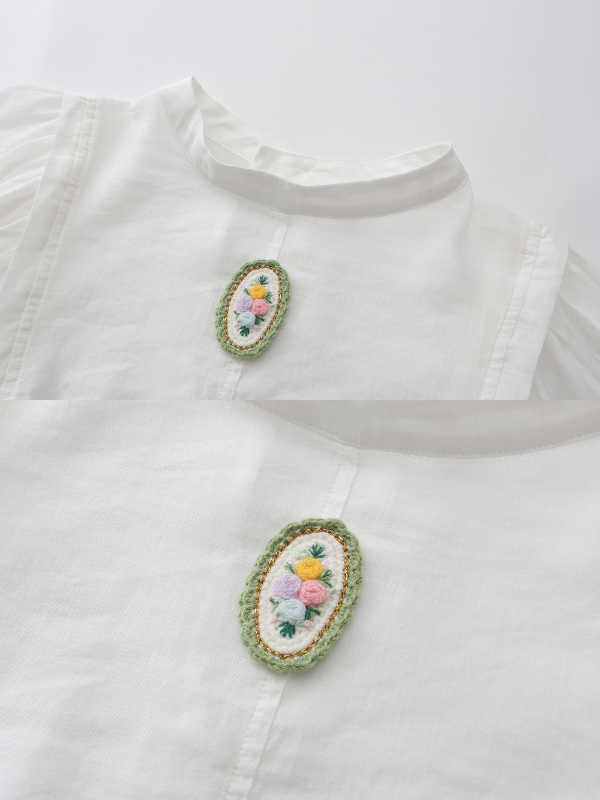 Close-up of a white blouse with an embroidered floral brooch, highlighting delicate stitching and soft fabric for a cottagecore aesthetic outfit.