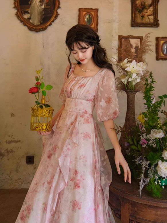 A vintage-inspired floral dress with layered ruffles and a square neckline, styled with a delicate gold birdcage, evoking a fairytale aesthetic.