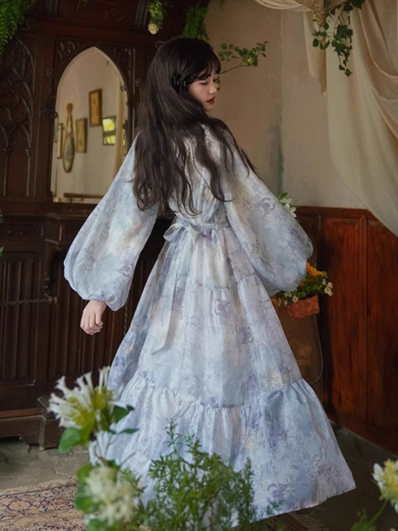 Back view of a flowing lavender floral dress with a tied waist and billowy sleeves, capturing a dreamy, ethereal vibe in a vintage-inspired setting.