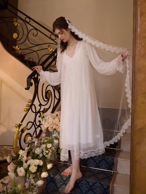 A young woman walks gracefully down a floral staircase in a romantic white slip dress and sheer lace gown, embodying a dreamy fairytale mood.