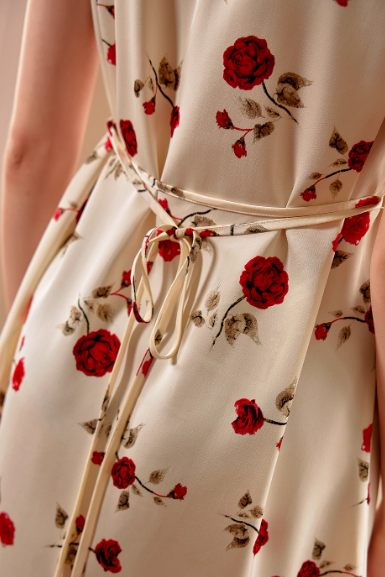 Close-up of the cream floral dress showing a delicate waist tie and vivid red rose print, blending romantic vintage style with cottagecore charm.