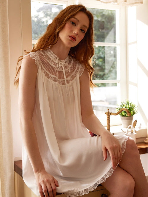A red-haired model sits by the window in a romantic white lace nightgown with a ruffled hem and sheer collar, radiating soft princesscore elegance.