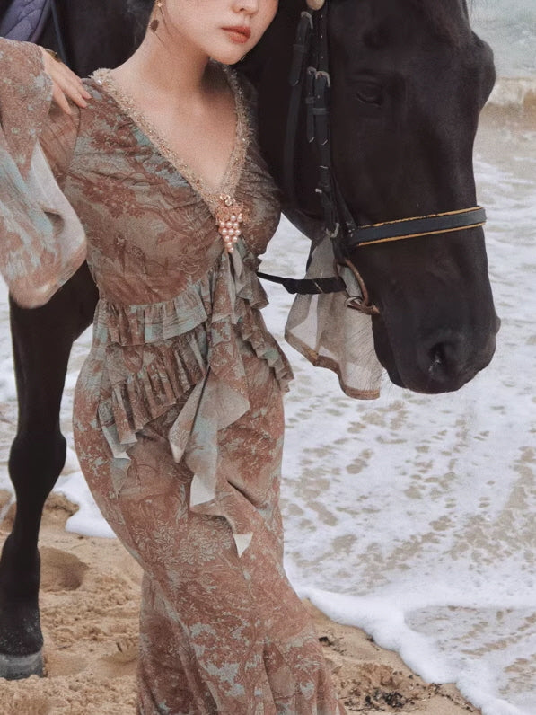 Model wearing a Romantic Fairytale vintage floral maxi dress with lace-trim V-neck, cascading ruffles, and sheer bell sleeves beside a black horse on the beach, styled for a fairycore vintage aesthetic outfit.