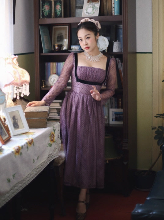 Model wearing a Romantic Fairytale vintage lavender polka dot maxi dress with a square neckline, sheer long sleeves, and black contrast trim, styled indoors in a cozy cottagecore vintage room.