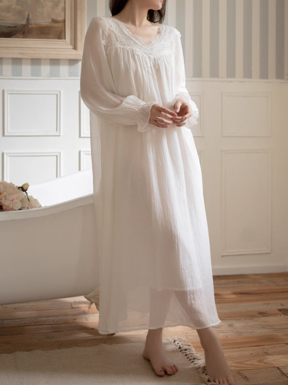 Model wearing an ivory lace yoke V-neck long nightgown with sheer long sleeves and a flowy vintage silhouette, romantic cottagecore loungewear in a bright bathroom setting.