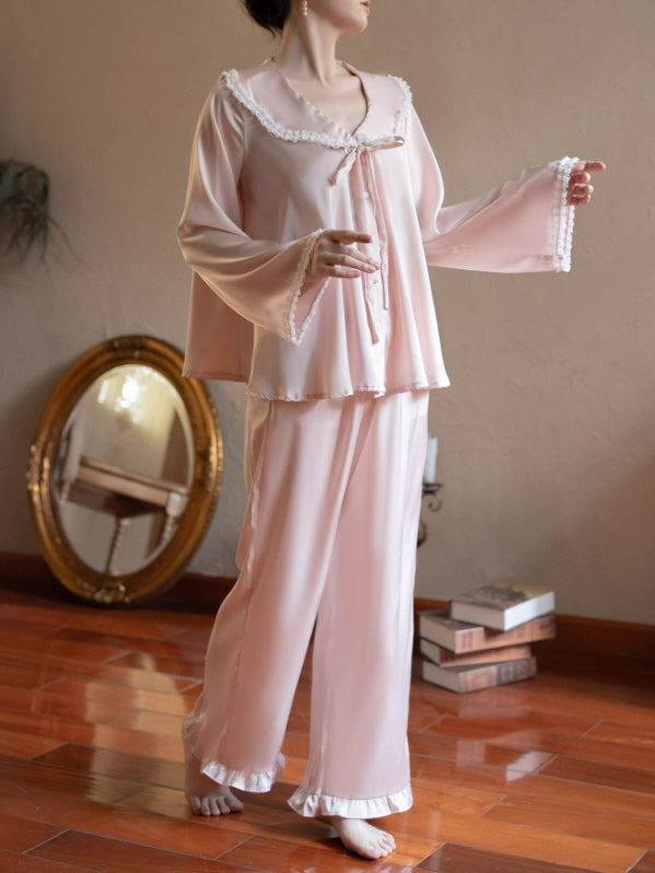 Model wearing a blush pink lace collar ribbon loungewear set with long sleeve top and wide-leg pants, vintage coquette cottagecore pajama outfit in a warm indoor room.