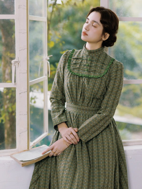 Model in a green checked prairie dress reading a book by an open window, highlighting the ruffled high neckline and soft fairycore vintage mood.