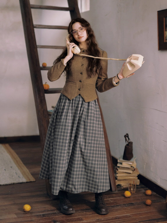 Woman wearing a brown vintage jacket paired with a long grey check skirt, holding a cream rotary phone in a cozy rustic room styled with books and wooden furniture, cottagecore aesthetic