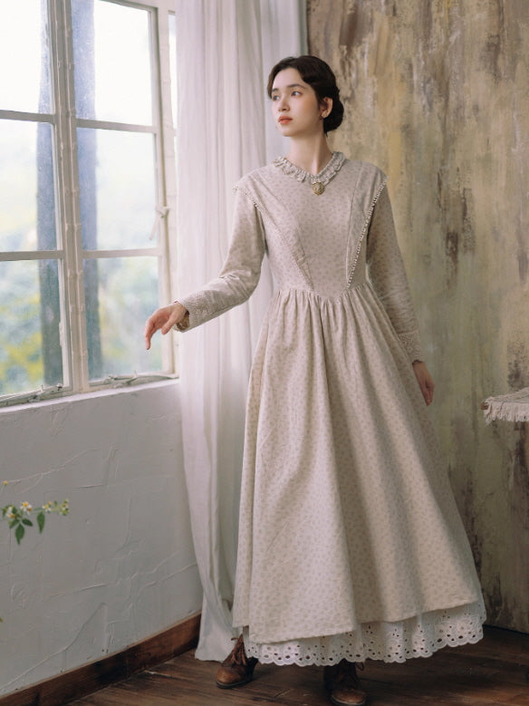 Vintage-inspired long beige dress with subtle floral pattern and lace hem, modeled indoors by a woman standing near a sunlit window, romantic cottagecore aesthetic outfit from Romantic Fairytale