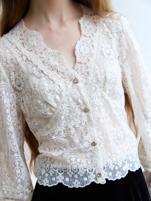 Close-up of an ivory floral lace blouse with crystal buttons and scalloped hem, showcasing its delicate fairytale aesthetic.
