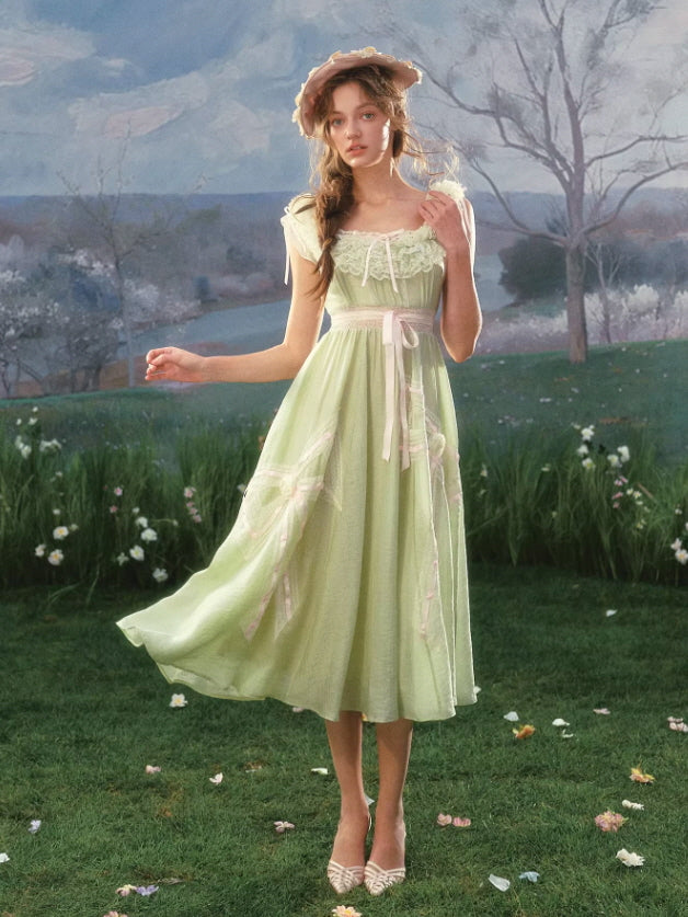 Romantic light green lace dress with ribbon waist detail and flowing skirt, styled in a meadow setting with a soft cottagecore and vintage fairytale aesthetic.