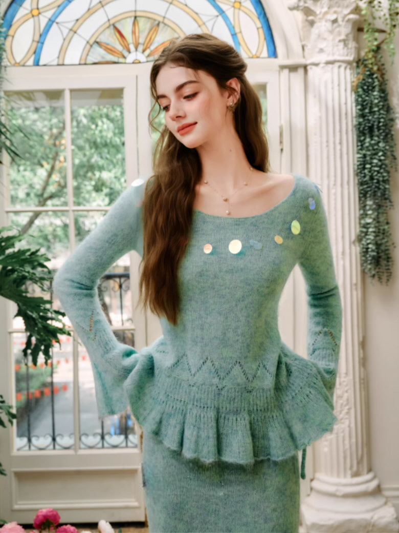 A soft mint green knit top featuring a delicate peplum hem, subtle pointelle knit texture, and shimmering sequin accents along the neckline, styled in a romantic vintage greenhouse setting.