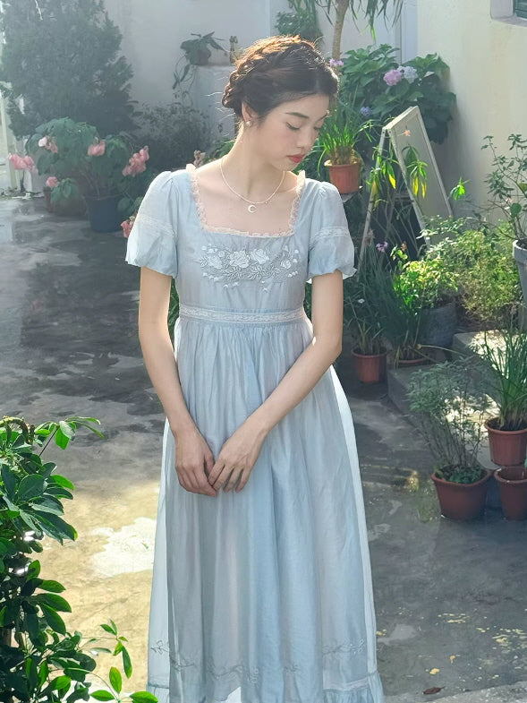 Front portrait of a woman in a light blue Regency-inspired empire waist maxi dress, showcasing an elegant vintage silhouette and soft fairytale vibes.