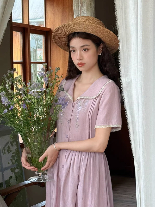 Front view of a romantic mauve midi dress featuring a lace-trimmed collar, button-down front, and delicate purple flower embroidery.