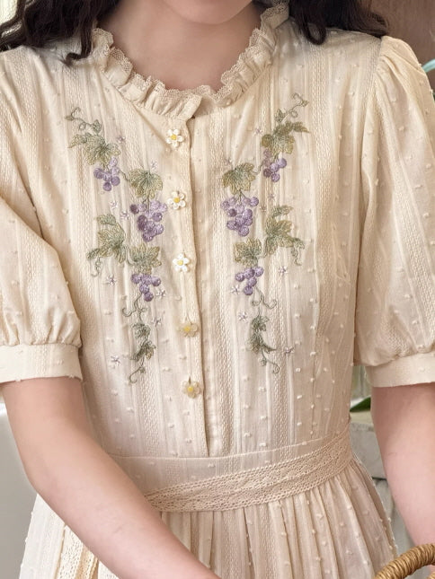 Close-up of ivory cottagecore dress featuring intricate purple grape embroidery and dainty white flower buttons.