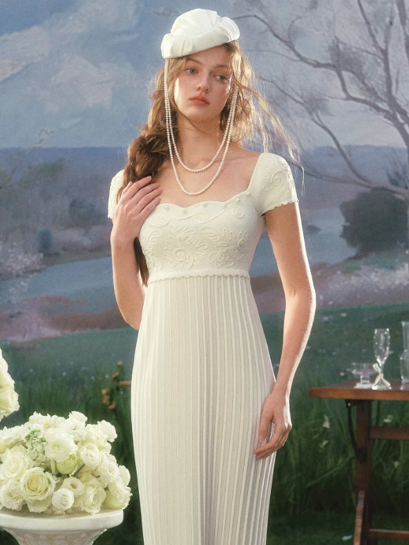 Soft romantic white dress with textured floral bodice and flowing pleated skirt, styled with pearl necklace and beret