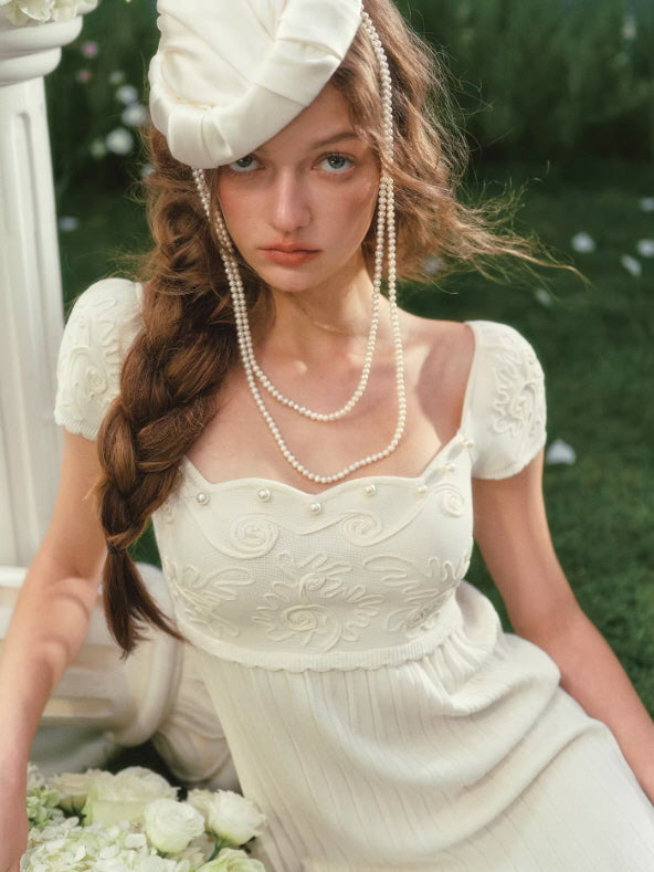 Close-up of embroidered ivory dress bodice with delicate floral patterns and pearl accessories, feminine vintage aesthetic
