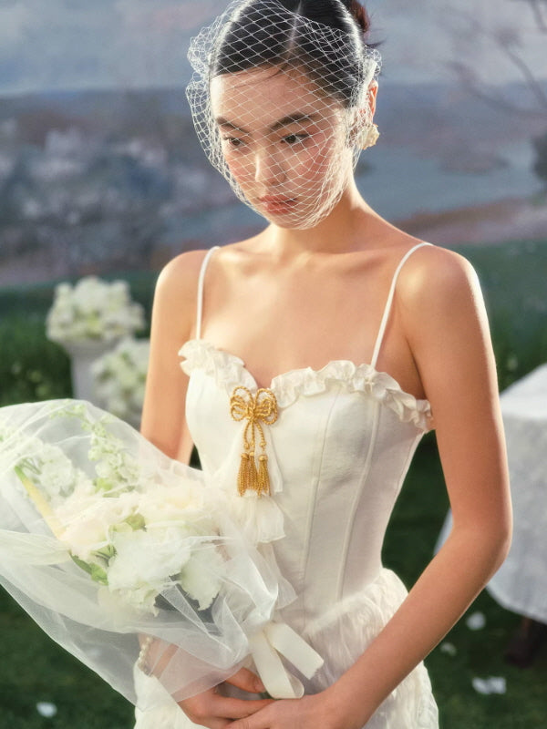 Close-up of ivory corset bodice with ruffle trim and gold bow embellishment, soft romantic bridal aesthetic
