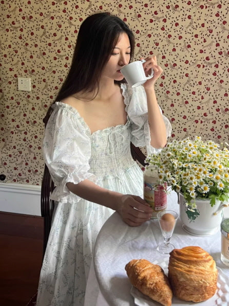 woman drinking tea in vintage room wearing cottagecore floral dress, soft morning aesthetic
