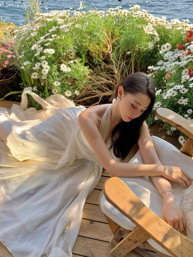 Romantic ivory goddess fairycore dress with halter neckline and flowing skirt among seaside flowers