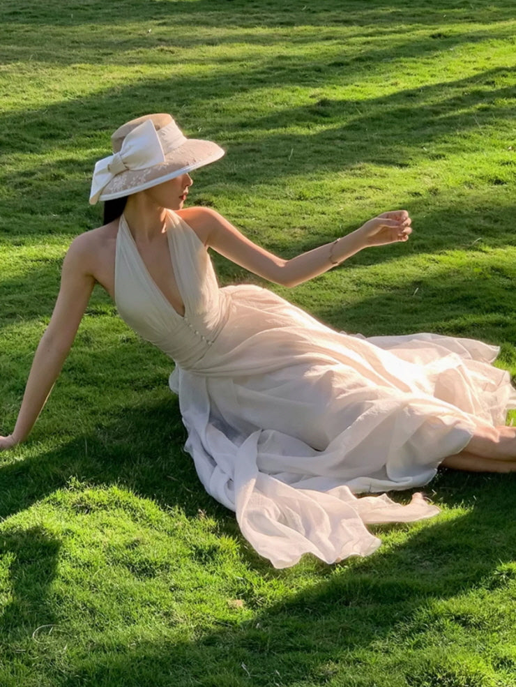 Ivory halter maxi dress with flowing sheer skirt and wide-brim hat on green grass