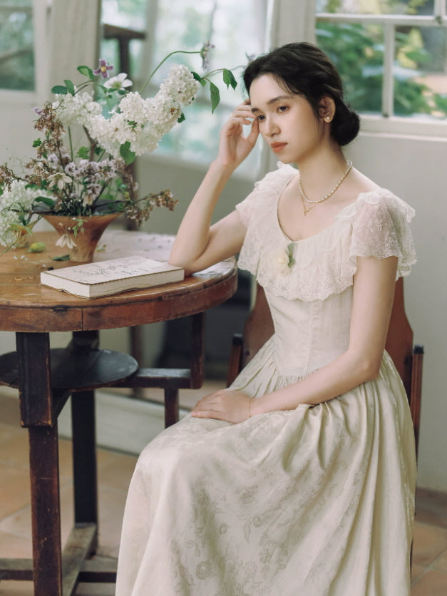 Dreamy ivory vintage maxi dress with delicate lace neckline, fitted bodice and subtle floral jacquard skirt indoors