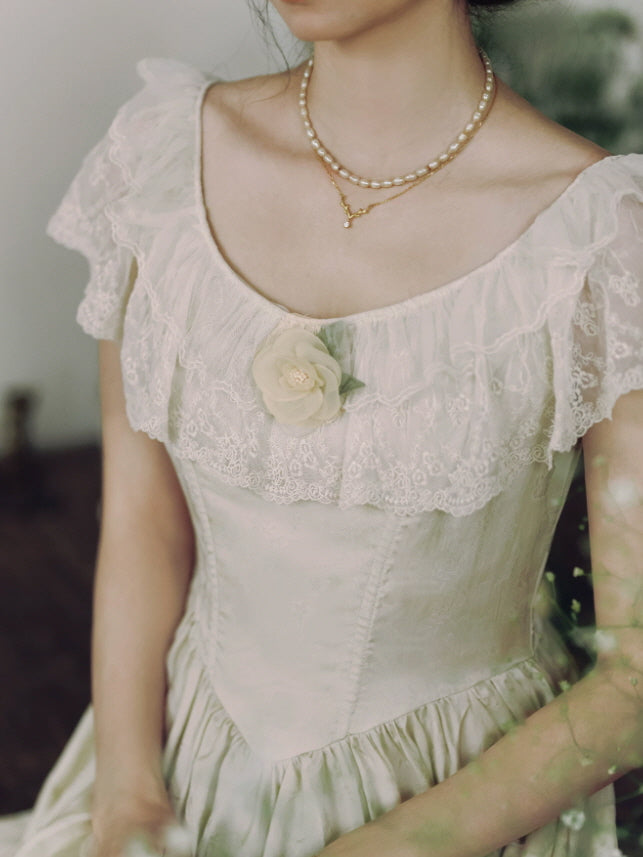 Close up of ivory cottagecore dress featuring embroidered lace ruffles, floral applique and fitted vintage bodice