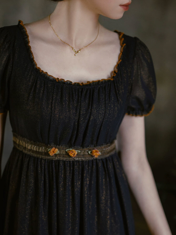 Close up of black puff sleeve dress featuring gathered square neckline, warm contrast trim and floral embroidered waist detail