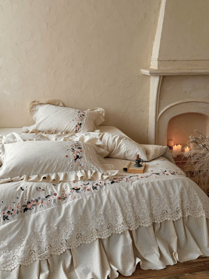 Romantic ivory bedding set featuring colorful wildflower embroidery, ornate lace details, and a flowing ruffle bed skirt