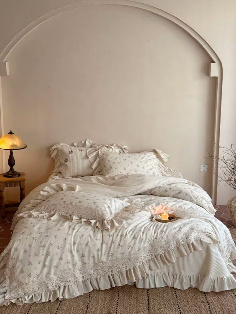Shabby chic bedding set featuring dainty floral patterns, ornate lace borders, and flowing ruffle details in soft ivory tones