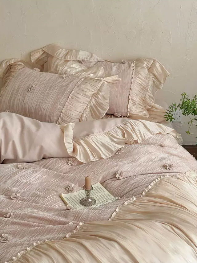 Shabby chic pink bedding with luxurious ruffled edges, floral appliques, and soft cream satin details in a feminine bedroom
