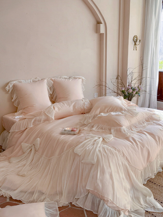 Blush pink bow ruffle bedding set with flowing ivory pleated trim in a romantic bedroom
