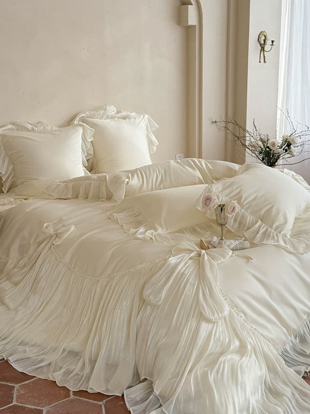 Close-up of cream bow bedding with glossy pleated ruffles and layered pillow trim
