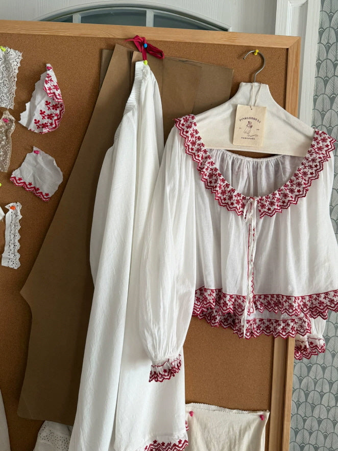 White cotton loungewear top with red embroidered lace trim, front tie and long gathered sleeves