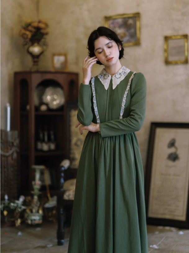 Green cottagecore maxi dress with fitted bodice, lace collar and flowing skirt styled beside wooden doors