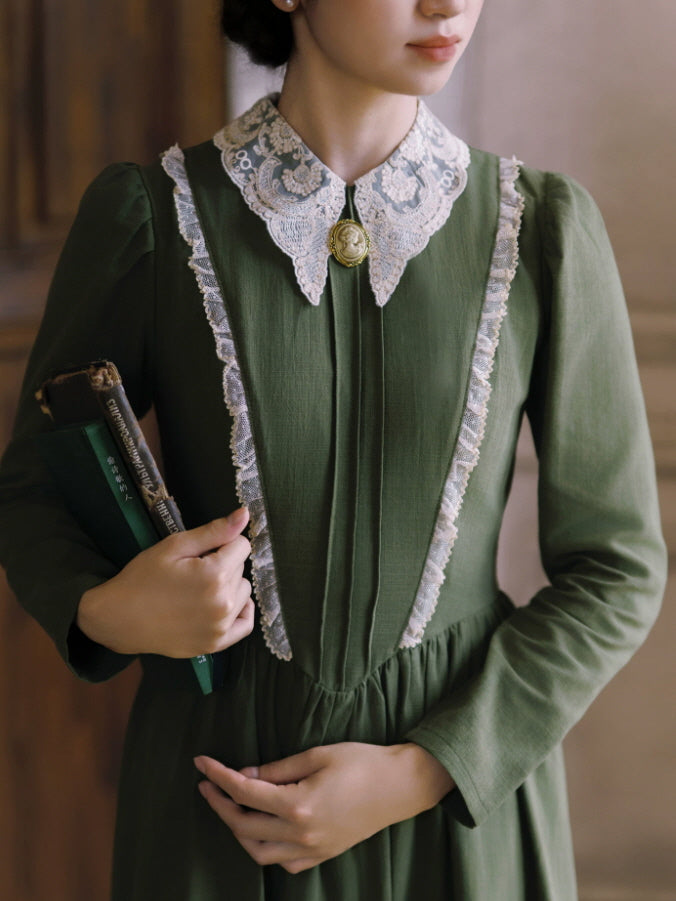 Close-up of green vintage dress with ornate white lace collar, cameo brooch and lace-trimmed bodice